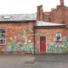 brick wall covered in mosaic flowers, birds, butterflies and bugs.  school project